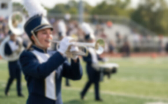 Young female marching band member playing trumpet during a halftime performance on a football field