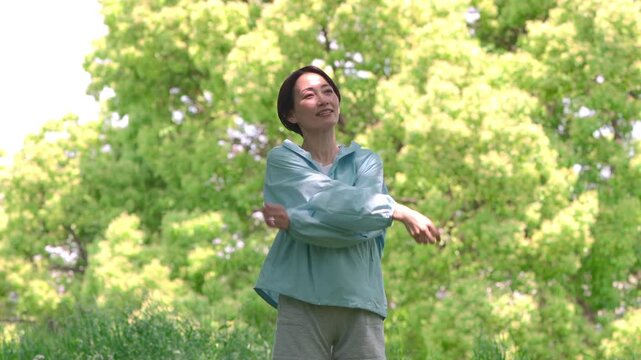 新緑の前で腕をクロスして腕のストレッチをする女性