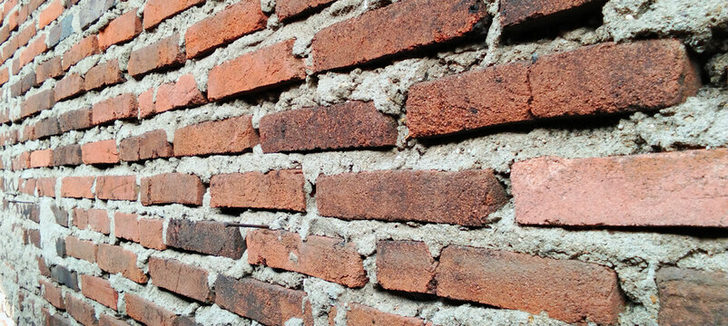 Rustic red brick wall texture against a rough cement mortar background.
