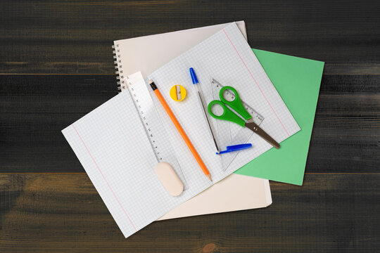School stationery as checkered notebook, scissor, pencil with eraser, pen with cap, ruler, eraser and pencil sharpener. On wooden surface background. File with Clipping Path.
