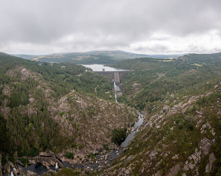 Aerial view of Encoro de Santa Uxia dam set within a rugged landscape of forested hills and rocky riverbanks under a cloudy sky in A Coruna, A Coruna, Spain.