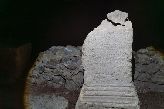 Ancient Greek stone stele with carved inscription dramatically lit in dark underground archaeological site in Turkey