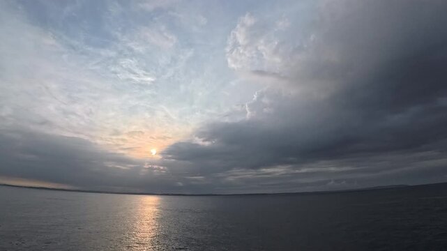 Cinematic real-time wide angle video of sun breaking through dramatic clouds over ocean with golden reflection path