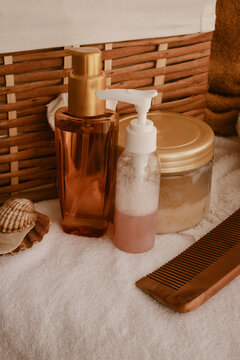 Spa day essentials arranged on a white towel. Including golden-capped bottles with skincare products. A foaming cleanser. A wooden comb. And seashells