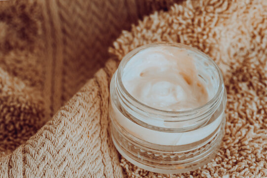 Open jar of white cream on a soft beige towel, conveying a sense of relaxation, self care, and wellness, perfect for beauty, skincare, and spa concepts