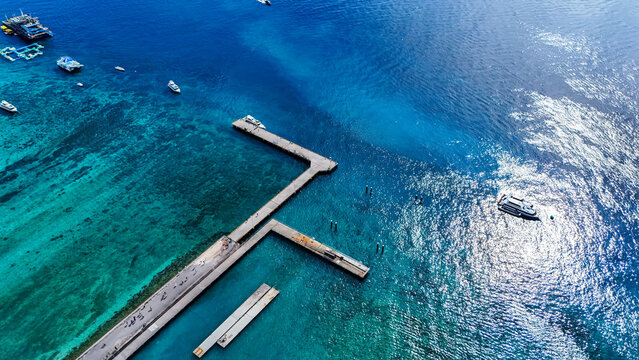 Aerial view of Banjar Nyuh Harbour with boats moored in the turquoise waters of the Indian Ocean, featuring concrete piers and clear tropical sea in Nusa Penida, Bali, Indonesia.