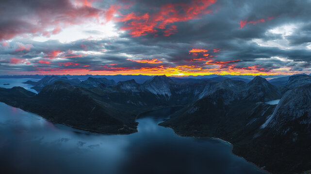 Aerial view of the iconic Stetind mountain peak rising above the deep blue waters of the fjord during a vibrant sunset in Narvik Municipality, Nordland, Norway.