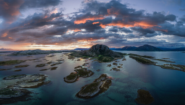 Aerial view of Torghatten mountain with its iconic hole at sunset, surrounded by coastal islands and dramatic clouds in Bronnoy Municipality, Nordland, Norway.