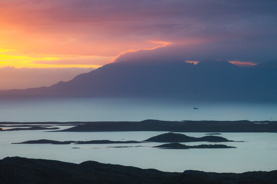 Aerial view of Torghatten mountain rising above the coastal islands and calm waters during a vibrant sunset in Bronnoy Municipality, Nordland, Norway.