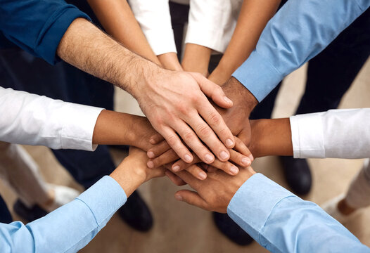 Diverse group of people putting their hands together in unity and teamwork during a meeting