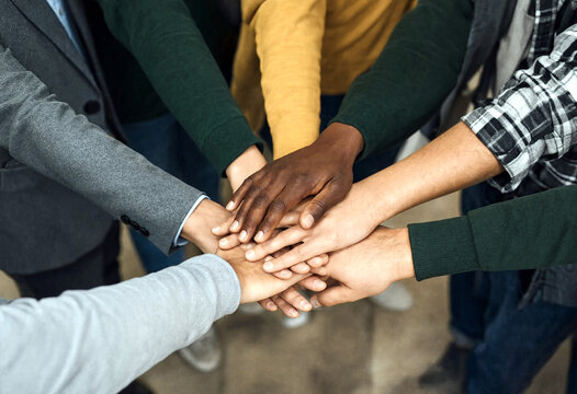 Diverse group of people putting their hands together in unity and teamwork gesture for collaboration