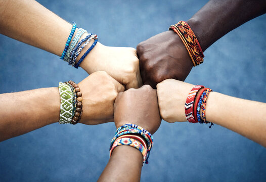 Diverse group of people showing unity with stacked hands wearing colorful friendship bracelets together outdoors