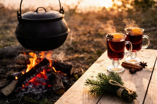 Hot mulled wine glasses near campfire with steaming pot ideal for winter camping food menu travel blog and cozy beverage advertising