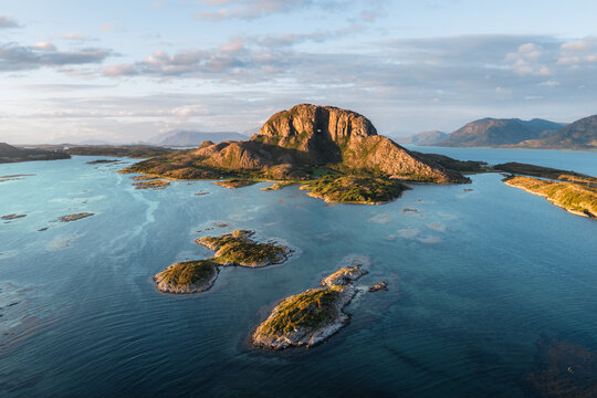 Aerial view of Torghatten mountain with its iconic natural tunnel, surrounded by small islands and the clear blue waters of the Norwegian coast in Bronnoy Municipality, Nordland, Norway.