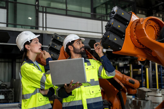 Engineers collaborating inspecting industrial robotic arm in factory