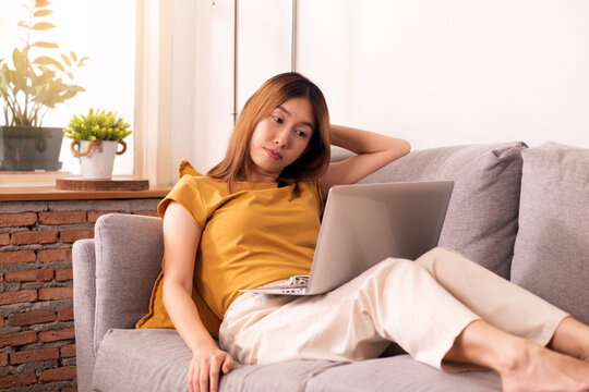 Tired woman working from home on laptop, experiencing work fatigue from prolonged screen time and sedentary work on a sofa.