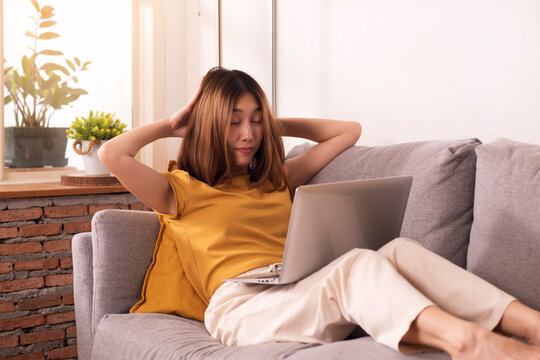 Tired woman working from home on laptop, experiencing work fatigue from prolonged screen time and sedentary work on a sofa.
