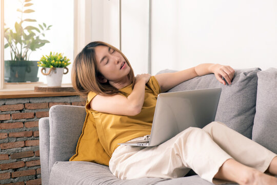 Tired woman working from home on laptop, experiencing work fatigue from prolonged screen time and sedentary work on a sofa.