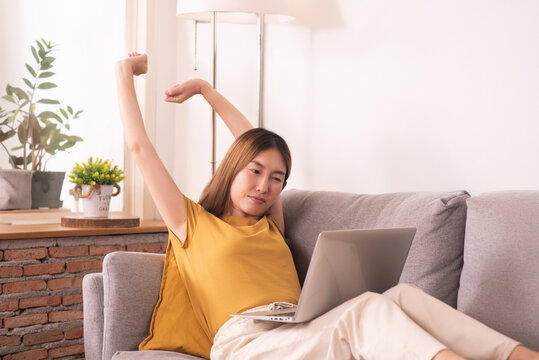 Tired woman working from home on laptop, experiencing work fatigue from prolonged screen time and sedentary work on a sofa.