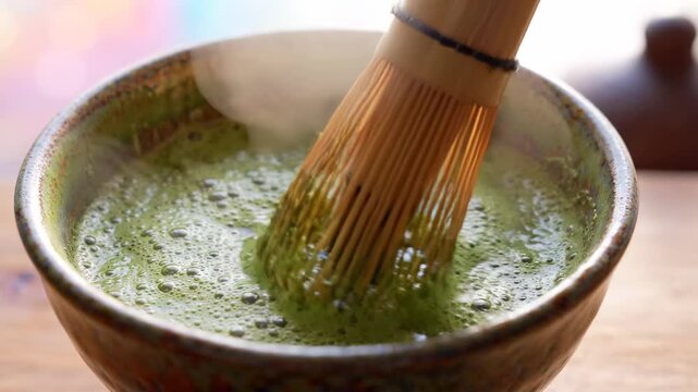 Japanese matcha tea preparation with bamboo whisk in ceramic bowl, frothy green beverage, steam rising, traditional ceremony, focus on texture and process