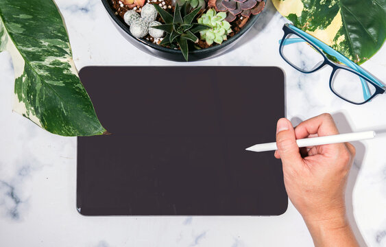Mockup concept showing hand holding smart pen over isolated black tablet screen on marble background, real image, not AI generated.