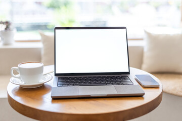 Fototapeta premium A blank screen laptop, coffee cup and smartphone placed on a round wooden table in a bright indoor space.