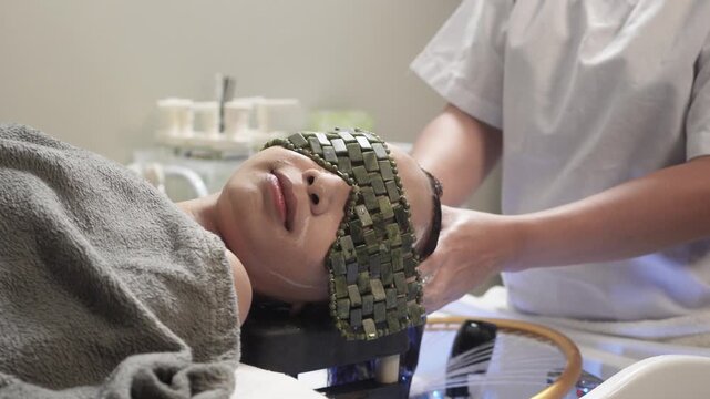 Japanese head spa therapist shampooing a woman&rsquo;s hair while she relaxes with a cooling jade stone eye mask and water halo treatment.
