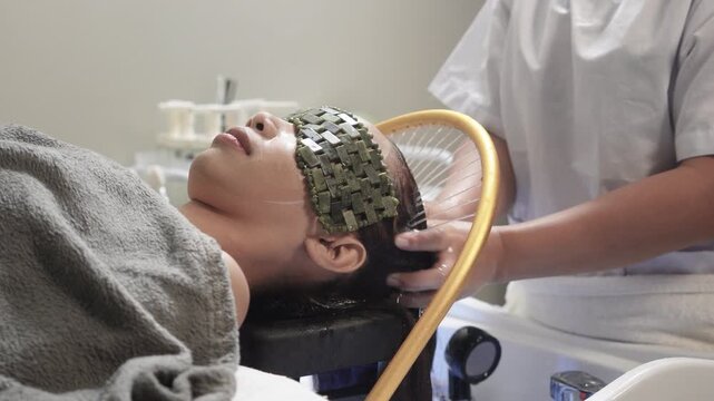 Japanese head spa therapist washes a woman&rsquo;s hair while she relaxes with a cooling jade stone eye mask and water halo treatment.