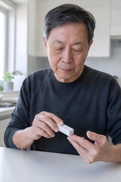 Senior chinese man using a block buffer to smooth his fingernails sitting at a table at home