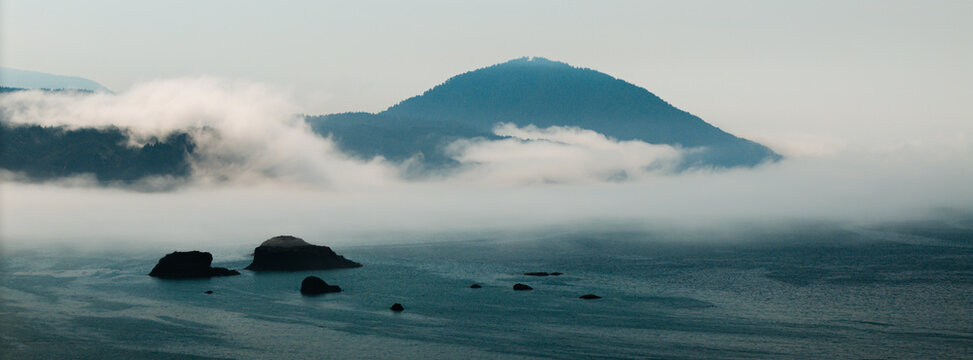 Aerial view of Port Orford, Oregon coastline with sea stacks, coastal fog, and Humbug Mountain in the background.