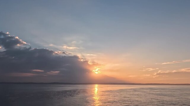 Cinematic real-time wide angle video of vibrant sun breaking through clouds with bright golden reflection path over ocean