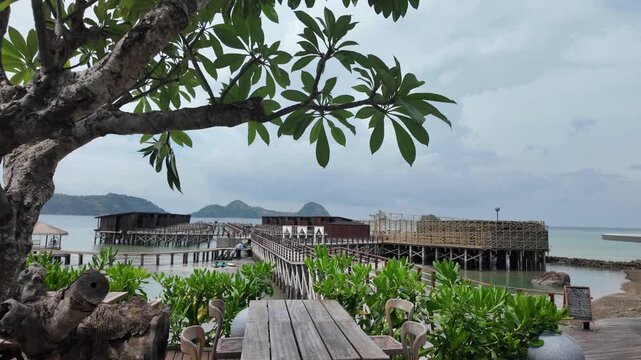 Scenic tropical resort with wooden pier and lush green trees overlooking the sea.