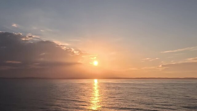 Cinematic real-time wide angle video of radiant sun breaking through clouds with bright golden reflection path over calm ocean