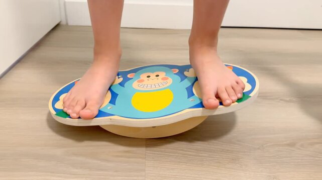A child standing on a colorful balance board at home, practicing balance and coordination. Indoor physical activity focused on motor skills, stability, body control, and healthy childhood development