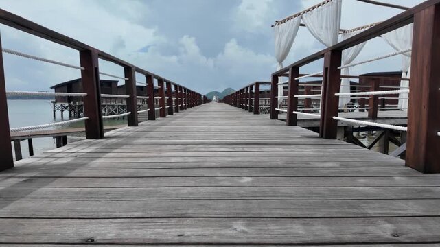 Wooden boardwalk leading towards luxury resort villas over water with cloudy sky.