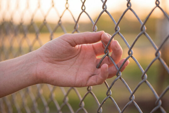 Human hand touching metal wires of a chain link fence
