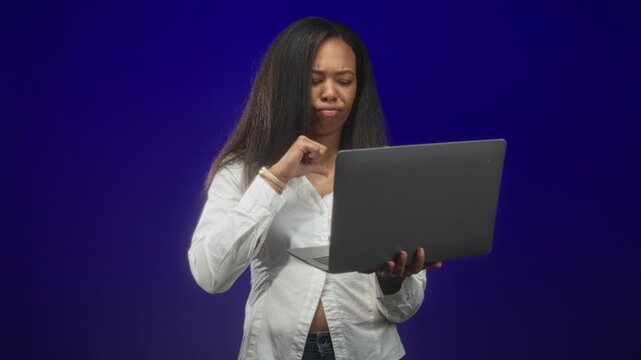 Woman holding laptop typing and making a thumbs down gesture in studio; frustration critique feedback.