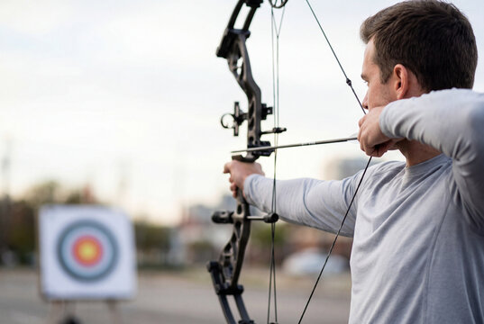 Male archer aiming a black compound bow towards a colorful target in the blurred background