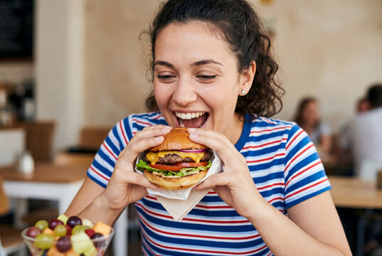 Cheerful young woman opening her mouth to bite a large burger