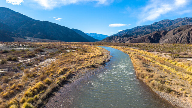 Aerial view of the San Juan river flowing through the arid landscape near the Ruinas de Planta de Sulfato de Aluminio, with rugged mountains in Calingasta, San Juan, Argentina.