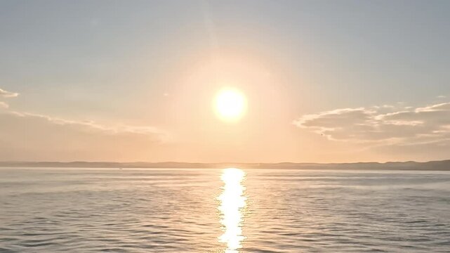 Cinematic real-time wide angle video of brilliant sun blazing over ocean with bold golden reflection path