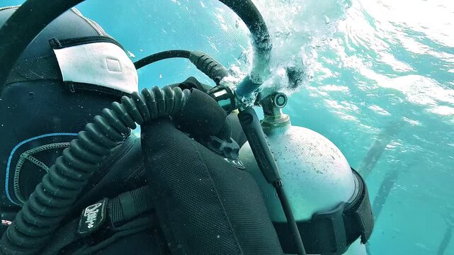 Close-up of an air leak from a scuba octopus hose behind a diver, with bubbles escaping from the damaged breathing system underwater.