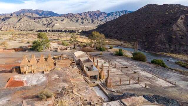 Aerial view of Ruinas de Planta de Sulfato de Aluminio, the historic industrial ruins set against a rugged mountainous landscape with a flowing river in Calingasta, San Juan, Argentina.