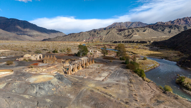 Aerial view of the historic Ruinas de Planta de Sulfato de Aluminio situated along a river in an arid mountainous landscape in Calingasta, San Juan, Argentina.