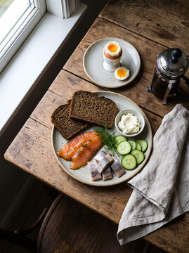 Nordic breakfast with smoked salmon, rye bread, eggs, and coffee is served on a rustic wooden table.