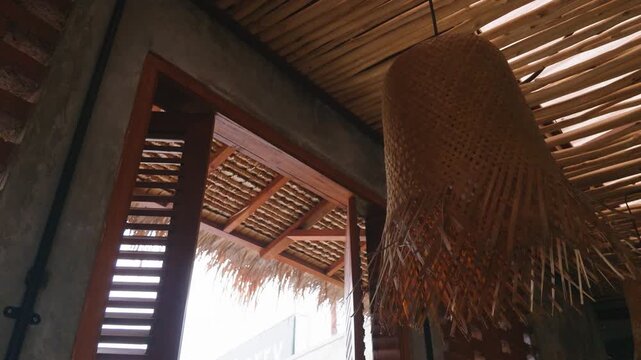 Rustic tropical interior design featuring a woven wicker lampshade and a wooden shutter window.