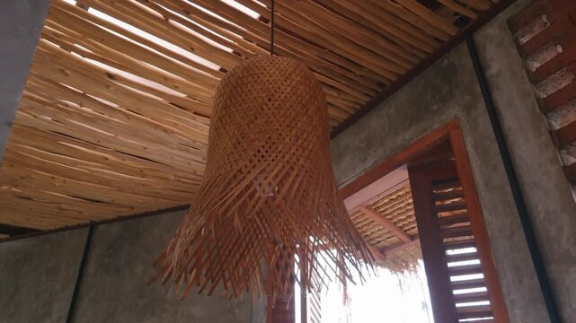Handmade woven rattan lampshade hanging from a rustic bamboo ceiling in a tropical room.