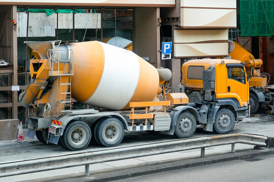 Industrial machinery rests near a city building zone while ready to transport wet concrete for heavy infrastructure projects during the middle of the day