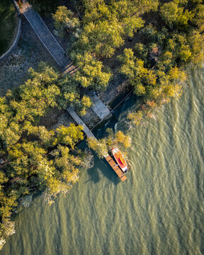 Aerial view of a small boat moored at a wooden pier on the shoreline of Lake Chapala surrounded by lush green trees in Ajijic, Jalisco, Mexico.