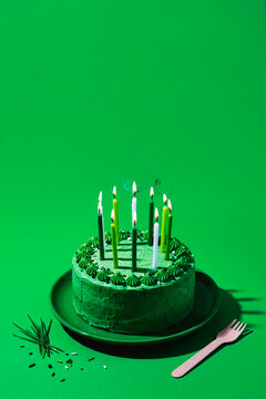 Green birthday cake with lit candles on a green background
